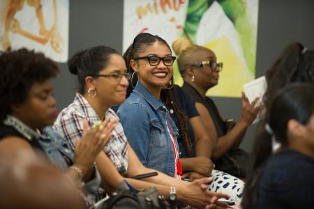 A young seated in a row with other students smiles.