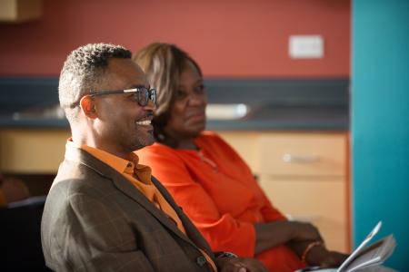 A man and woman sit next to each other listening to a speaker.